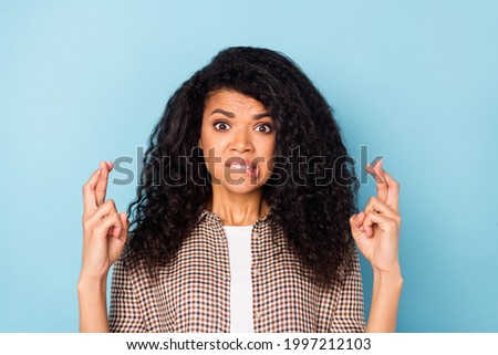 Photo of upset curly hairdo young lady crossed fingers bite lip wear brown shirt isolated on vivid blue color background
