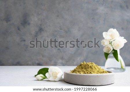 henna powder for dyeing hair and eyebrows and drawing Mehendi on hands on a gray cement pedestal with dried flowers or a white flower.