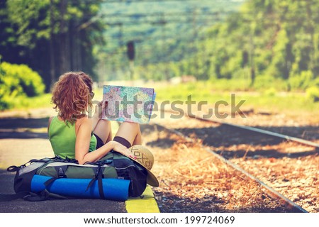 Girl wearing backpack holding map, waiting for a train. Royalty-Free Stock Photo #199724069