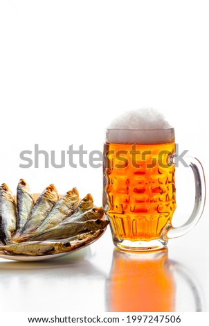 Mug of refreshing light beer with dried fish appetizer on a large white platter on a white plate