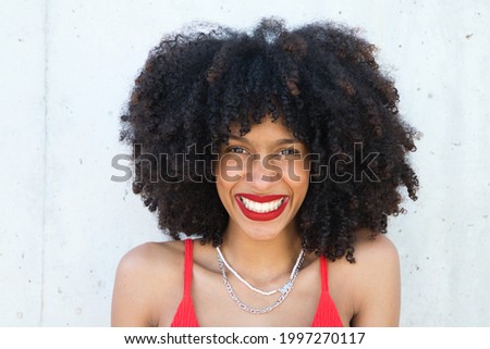 beautiful afro american woman smiling and looking at the camera doing different poses and gestures with her face. The woman is wearing a red top and red lipstick. Concept happiness Royalty-Free Stock Photo #1997270117