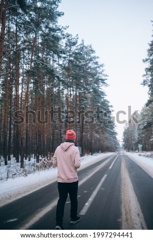 Guy standing on the road in the middle of the forest, surrounded by snow