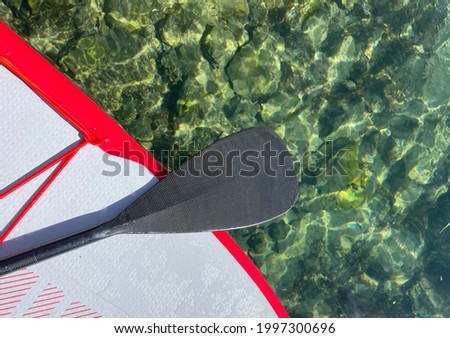 Black Paddle, white and red board and beautiful sea. Top view as background. Adventure, travel, healthy lifestyle, physical activity concept. Copy space for invitation or gift card.