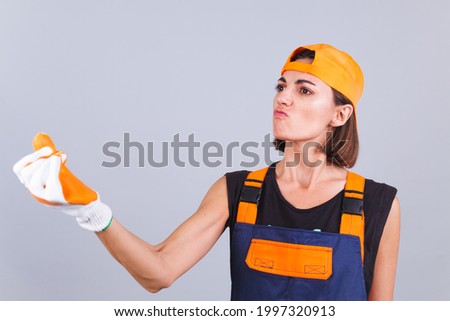 Painter worker woman in overalls and gloves on gray background angry disappointed swears