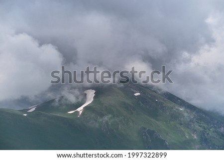 Forest and mountains in fog in cloudy weather. Beautiful landscape of National Park of Russia. Dark thundercloud envelops snowy mountain peak.