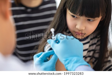 Asian  senior doctor wearing gloves and isolation mask is making a COVID-19 vaccination in the shoulder of child patient with her mother at hospital.closed up photo.