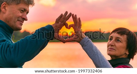 mature beautiful couple folded a heart with their hands on the background of the sunset on a summer evening