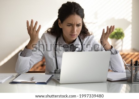 Angry female nurse work on laptop in clinic frustrated by slow internet connection on gadget. Unhappy mad woman doctor use computer in hospital confused with operational problem or spam on device. Royalty-Free Stock Photo #1997339480