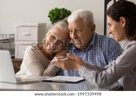 Female realtor or broker show house plan on computer to excited old middle-aged couple at meeting in office. Woman agent or consultant help mature spouses with bank loan or mortgage at briefing. Royalty-Free Stock Photo #1997339498
