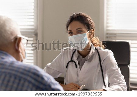Close up of female doctor in facemask against covid-19 coronavirus consult old male patient in clinic. Woman GP wear protective facial mask from corona virus talk with mature man. Healthcare concept.