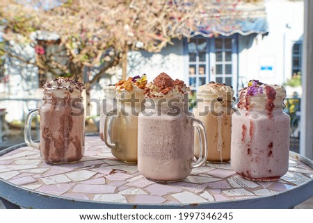 Gourmet milkshakes  displayed on a mosaic table with a vintage cottage-style restaurant in the background ( chocolate, honeycomb flavor , berry , peanut butter milkshakes )
