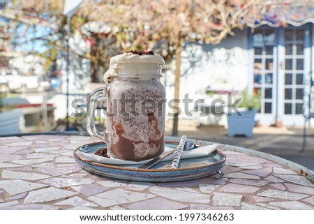 Gourmet milkshakes  displayed on a mosaic table with a vintage cottage-style restaurant in the background ( Chocolate flavor  milkshake )
