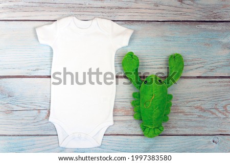 White baby bodysuit mockup with toy on wooden background. Styled stock photography. Mock up.