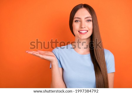 Photo of pretty long hairdo millennial lady hold empty space wear blue t-shirt isolated on orange color background