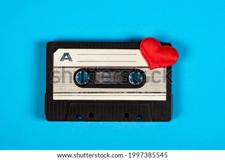 Old Audio Cassette with a Red Heart on the Blue Paper Background closeup