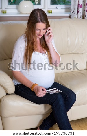 Attractive pregnant woman talking on phone whilst looking at ultrasound baby scan