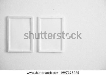 front view of two blank white vertical photo frames hanging on clean white cement wall and blank space in the right side position, interior design background concept.