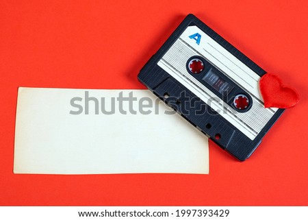 Old Audio Cassette with a Heart Shape and Blank Paper on the Red Background closeup