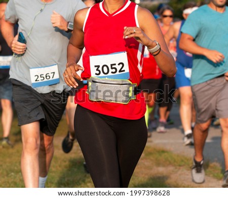 Close up of runners racing a 5K in a trail with a women wearing a fanny pack around her waist to carry her personal iteams. Royalty-Free Stock Photo #1997398628