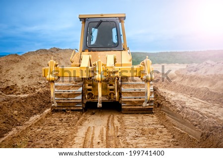 Bulldozer with steel blade moving soil and sand around and working in a sandpit on construction site of a house, road or industrial hall Royalty-Free Stock Photo #199741400