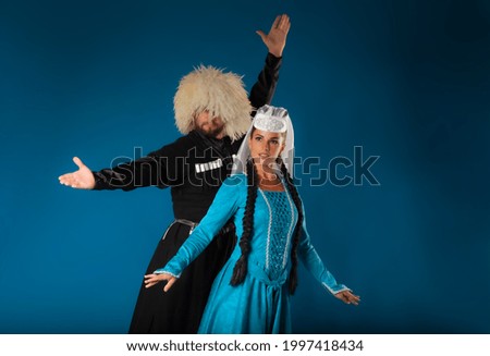 Energetic pose of Georgian couple of dancers in authentic costumes on blue backdrop. High quality picture of authentic Caucasian dancers performing on dark blue matte background