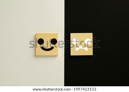 Wooden block emoticon use for Customer service satisfaction and evaluation over black and white paper split in half  background with  copyspace.,feedback,customer service,rating,Opposites concept