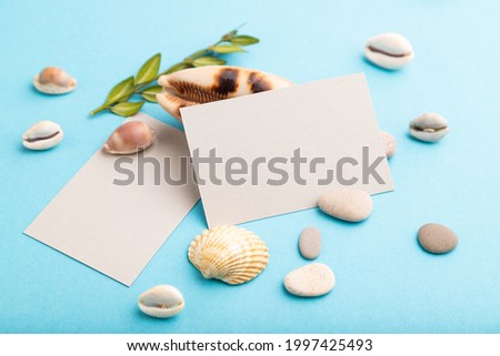 Composition with gray paper business cards, seashells, green boxwood. mockup on blue pastel background. Blank, side view, still life, copy space. travel concept.