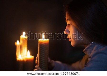 The girl looks at the burning candle two more candles are burning in the background