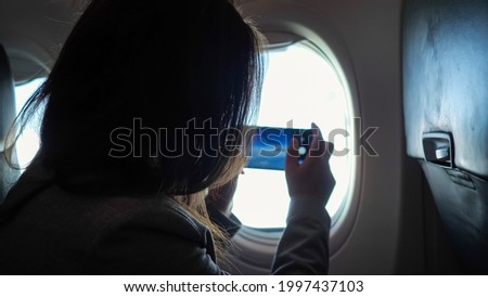 Unrecognizable woman photographs the view from the airplane window on the phone.
