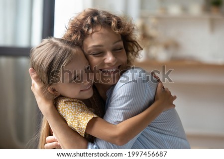 Affectionate caring happy young woman cuddling adorable smiling preschool adopted little kid girl, expressing love and devotion, missing after long separation, sincere family relations concept.