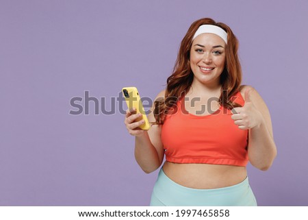 Young chubby overweight plus size big fat fit woman in red top warm up training hold yoga mat mobile cell phone show thumb up isolated on purple background home gym Workout sport motivation concept