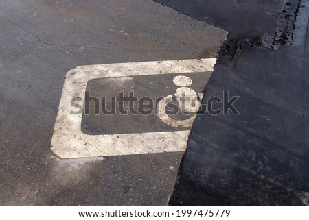 White lines on the asphalt after the rain. A parking space for the disabled in the parking lot, an icon, a sign drawn on a specially designated parking space for the disabled. Half of the sign is unde