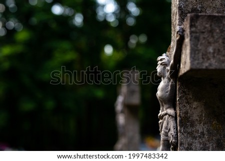 Jesus figurine on the cemetery cross. Picture taken in a soft light, shaded place.