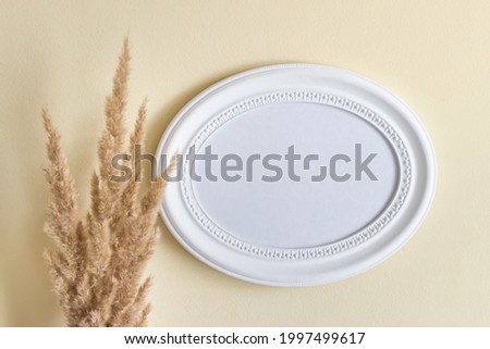 White oval blank wooden frame template with dry yellow field plant on the background of yellow wall.