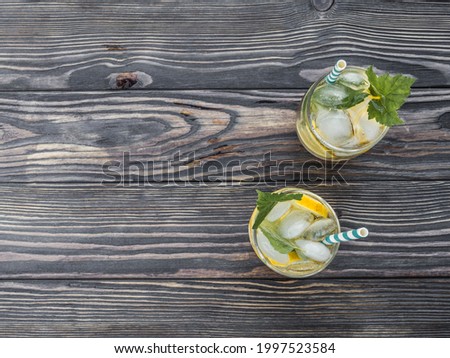 Lemonade with ice and currant leaves on a dark wooden table. Cold summer drink with paper cocktail tubes. View from above. Copy space.