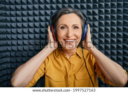 Hearing loss treatment. Positive mature woman wearing audiometry headphones while hearing test and audiogram in special audio room