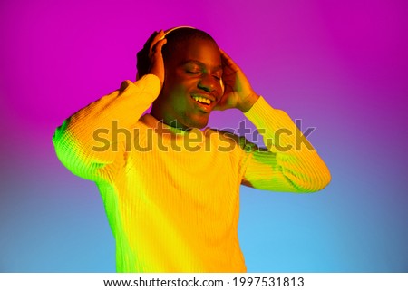 Yellow and magenta colors. Young happy African handsome man isolated over gradient background in neon light. Male fashion model in casual clothes. Concept of human emotions, facial expression, youth.