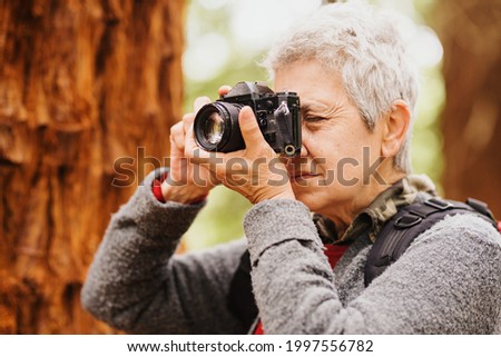 old woman with old film camera taking pictures in the forest. pensioner doing activities