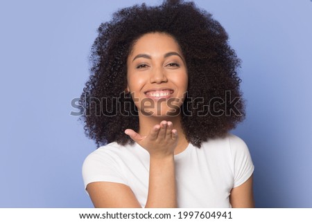 Headshot portrait of smiling millennial African American woman isolated on blue studio background send air virtual kiss. Profile picture of happy young mixed race female feel excited show love care.