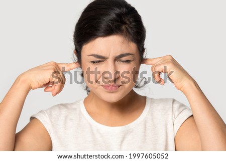 Irritated young Indian woman isolated on gray studio background close plug cover ears avoid ignore loud sound or noise. Bothered millennial mixed race female feel stressed annoyed by noisy neighbors. Royalty-Free Stock Photo #1997605052