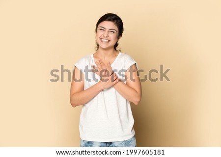 Portrait of smiling young Indian woman isolated on yellow studio background with hands on chest feel grateful thankful. Happy millennial mixed race female show care and support. Charity concept. Royalty-Free Stock Photo #1997605181