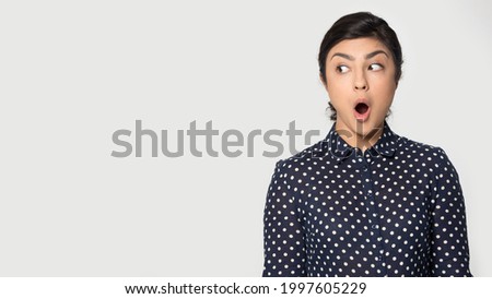 Stunned young Indian woman isolated on grey studio background look at empty copy space shocked by promotion or sale. Amazed mixed race female feel surprised by good discount offer online.