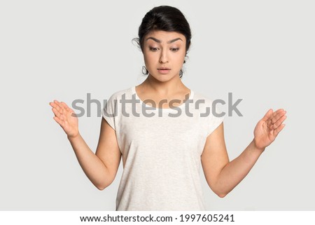 Stunned young Indian woman isolated on grey studio background show empty copy space with hands look at good deal or promotion ad. Millennial mixed race female demonstrate copyspace for advertising.