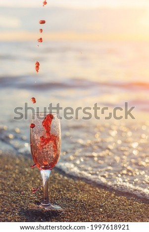 A tall glass with splashes of red wine on the seashore. Sunset