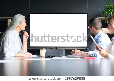 Global corporation online video chat business webinar in meeting room with multiethnic diverse colleagues in office watching big empty blank white screen monitor. Business technologies concept.