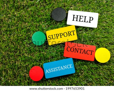 Text HELP SUPPORT CONTACT ASSISTANCE on colorful wooden board on green grass background.
