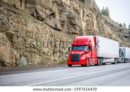 Group of big rigs semi trucks tractors transporting cargo in different semi trailers standing off road in a line near a stone cliff take a break at the pass on top of a mountain range in California Royalty-Free Stock Photo #1997656439