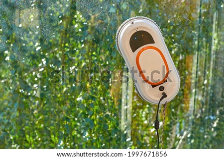 Smart Robotic Window Cleaner for Glass Cleaning. A robot vacuum cleaner cleans a dirty window against the background of tree foliage. The concept of cleaning and polishing windows.