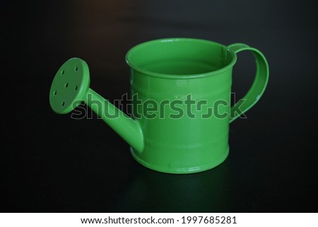 A mini green watering can in black background