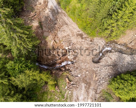 Aerial top down drone view, small flooded mountain creek flowing under the dirt road.